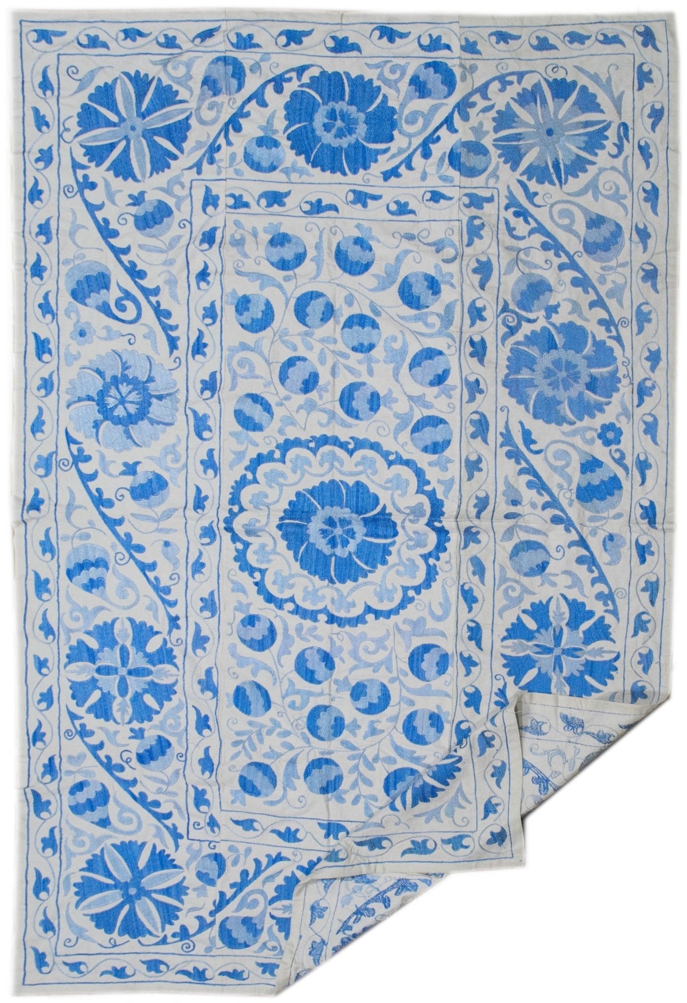 Handmade Uzbek suzani featuring blue floral and fruit embroidery on a white cotton base.