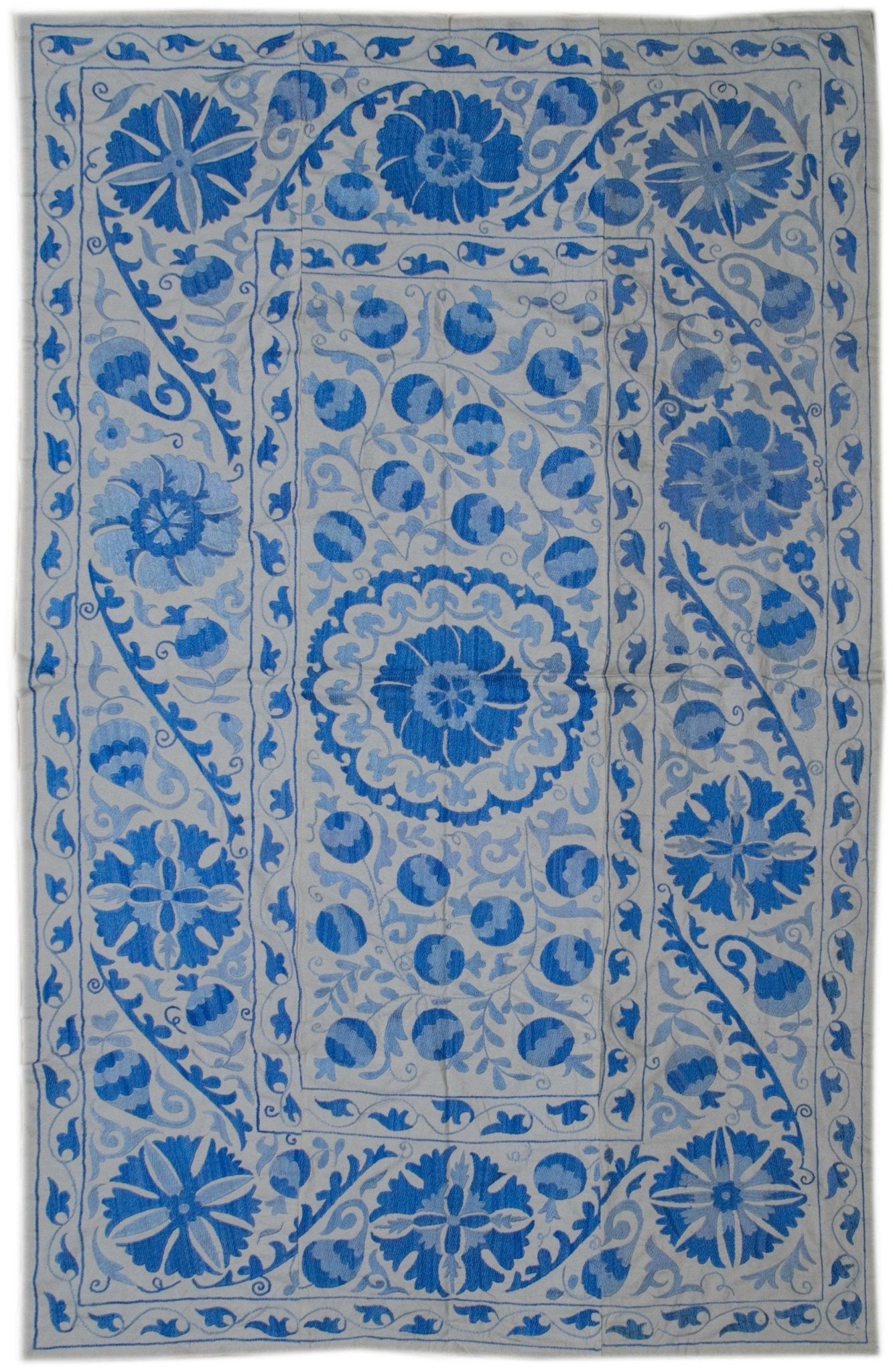 Handmade Uzbek suzani featuring blue floral and pomegranate embroidery on a white cotton base.