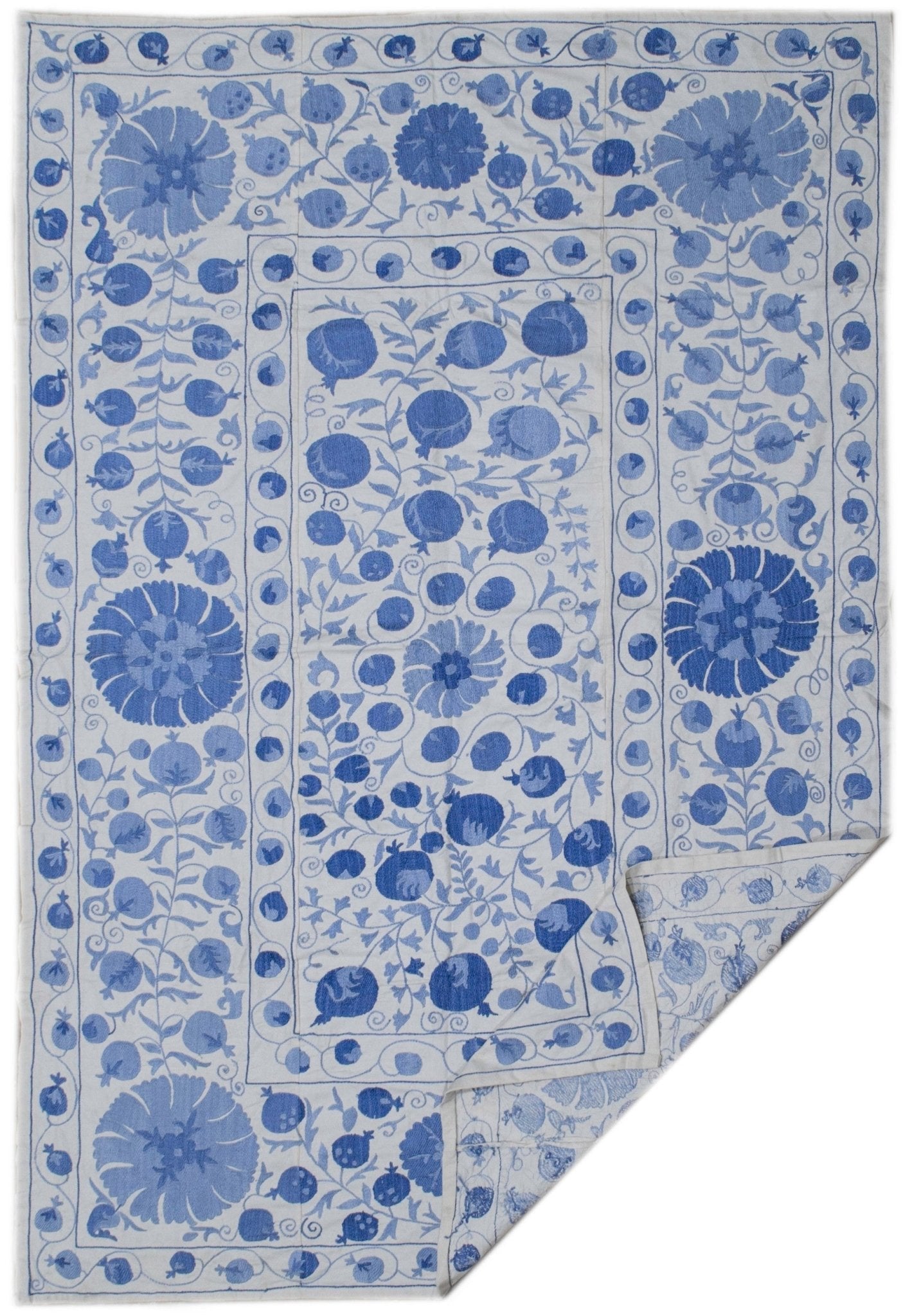 Handmade Uzbek suzani featuring blue floral and pomegranate embroidery on a white cotton base.