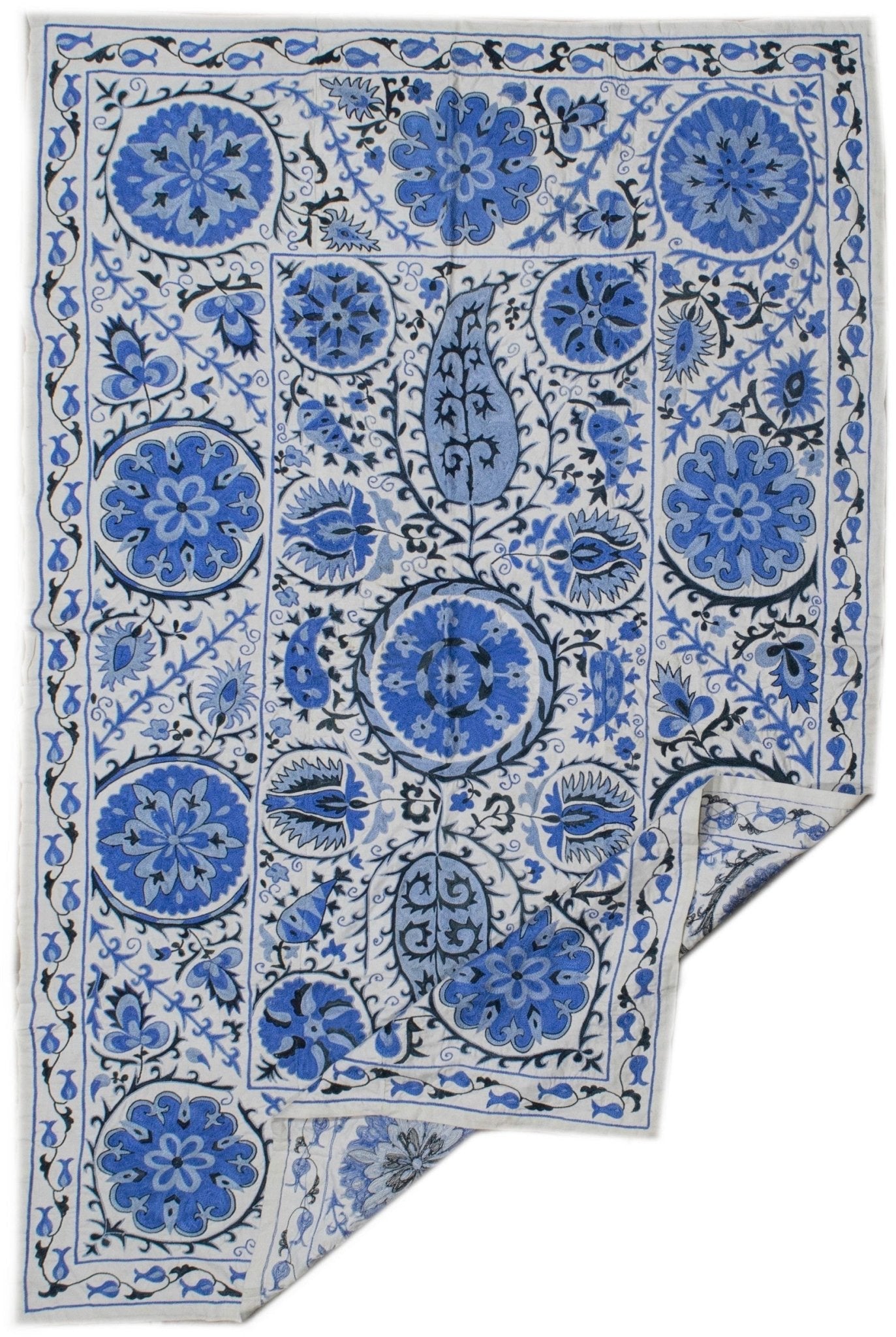 Handmade Uzbek suzani featuring blue floral and paisley embroidery on a white cotton base.