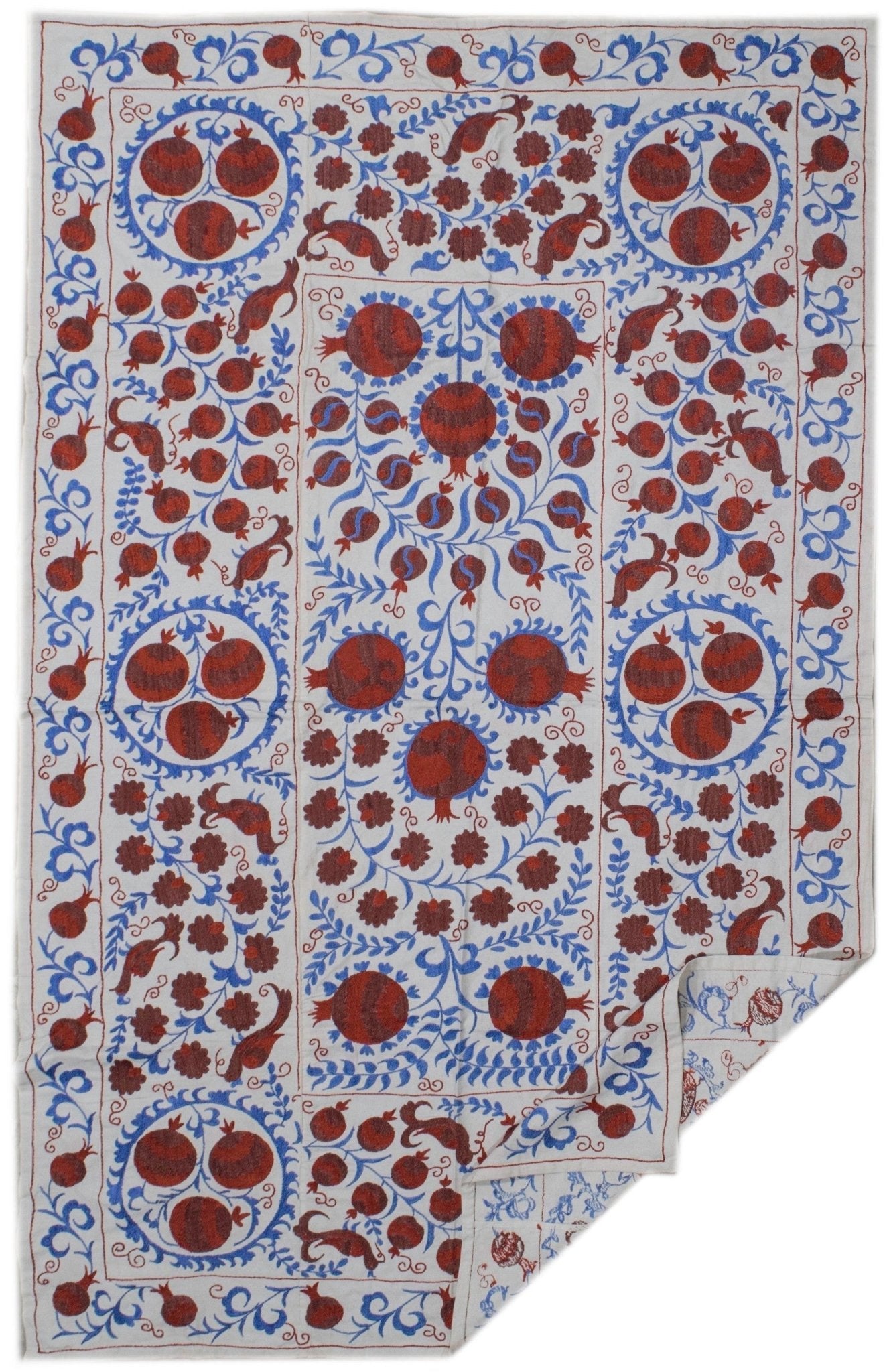 Handmade Uzbek suzani textile featuring intricate red pomegranate and blue floral embroidery.