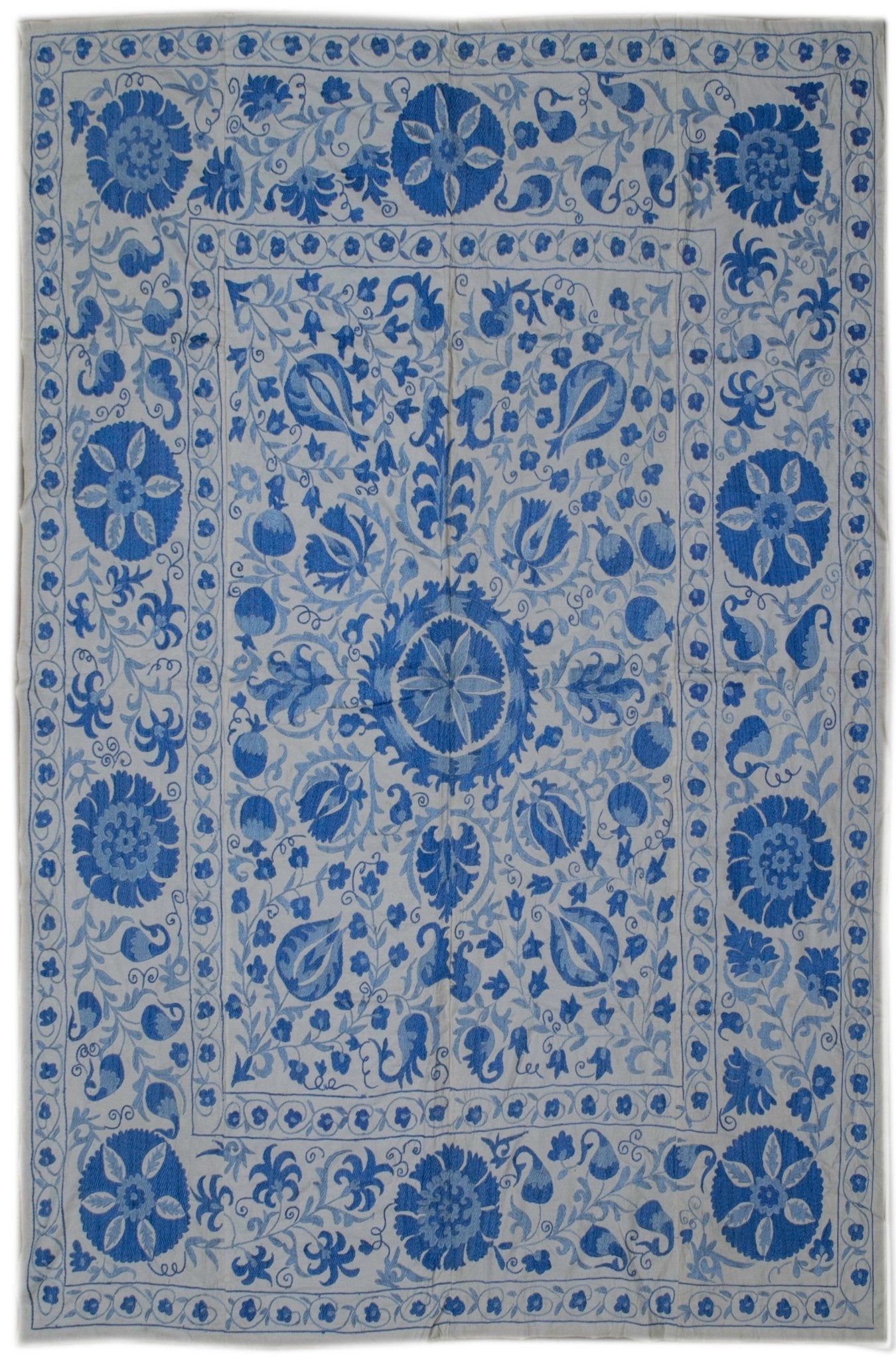 An Uzbek suzani featuring intricate blue floral and botanical embroidery on a light cotton base.