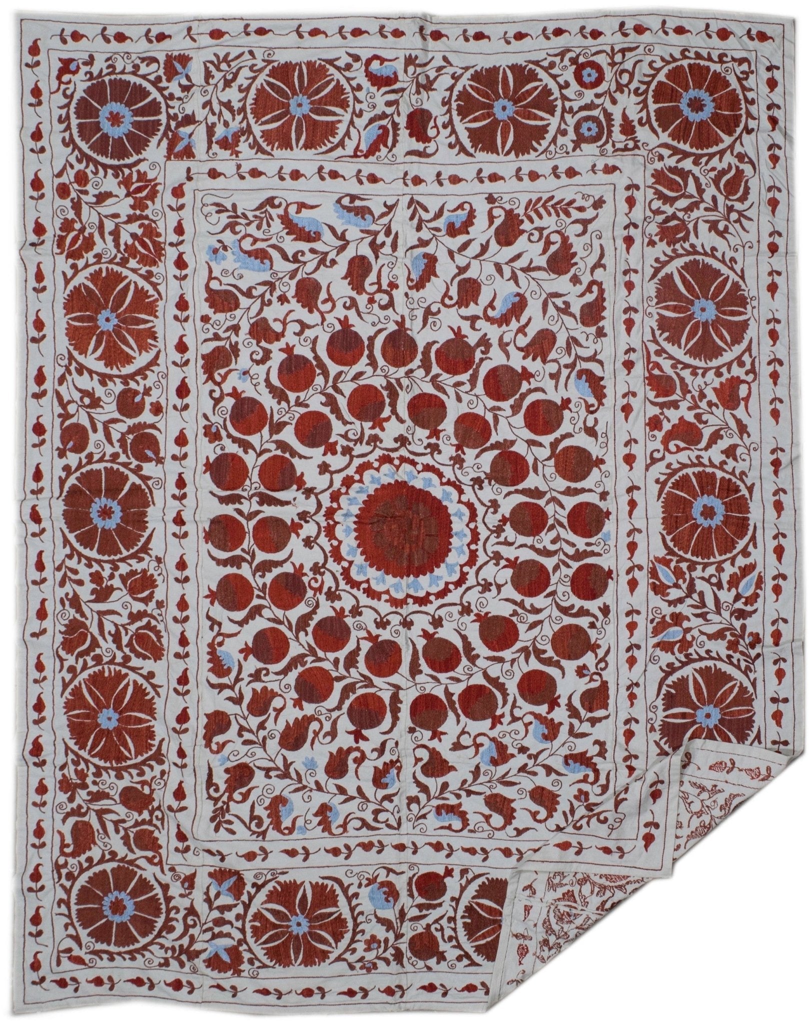 Hand-embroidered Uzbek suzani featuring red floral and pomegranate motifs on a white cotton base.