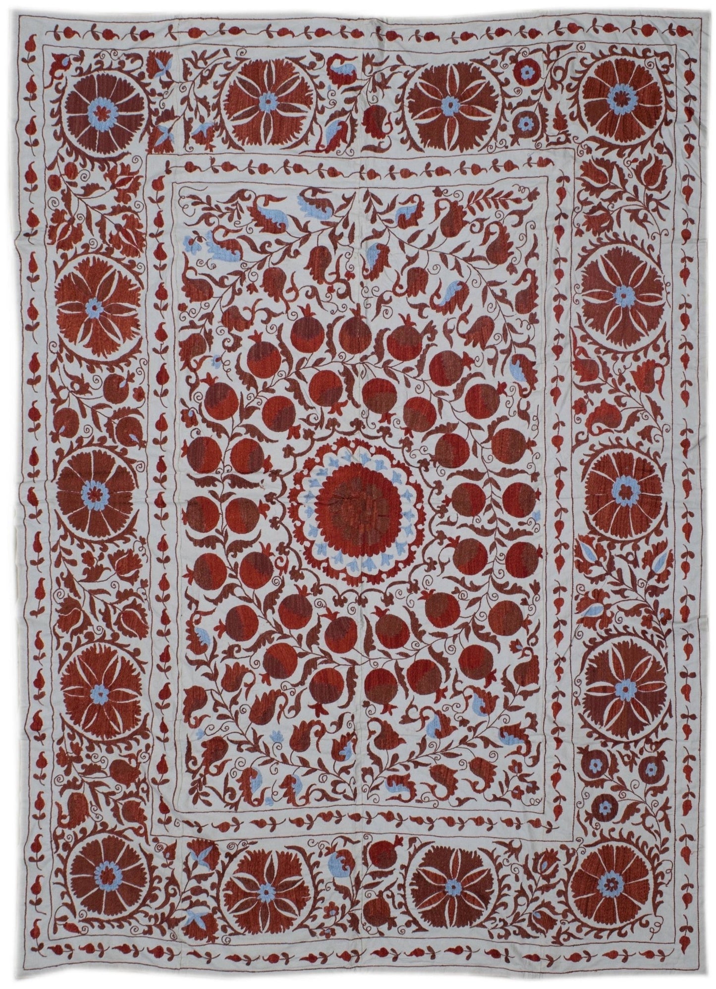 Hand-embroidered Uzbek suzani featuring red floral and pomegranate motifs on a white cotton base.