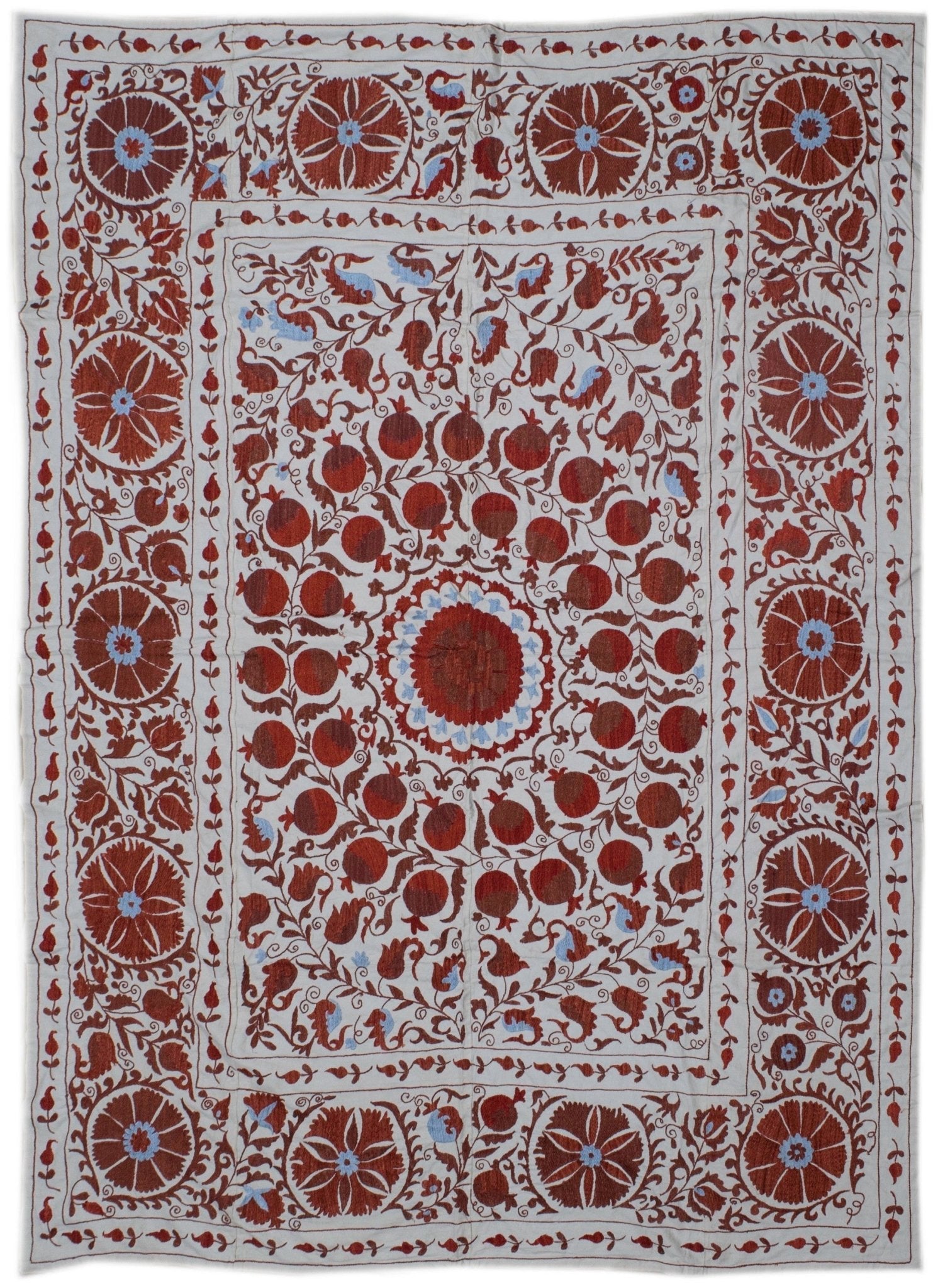 Hand-embroidered Uzbek suzani featuring red floral and pomegranate motifs on a white cotton base.