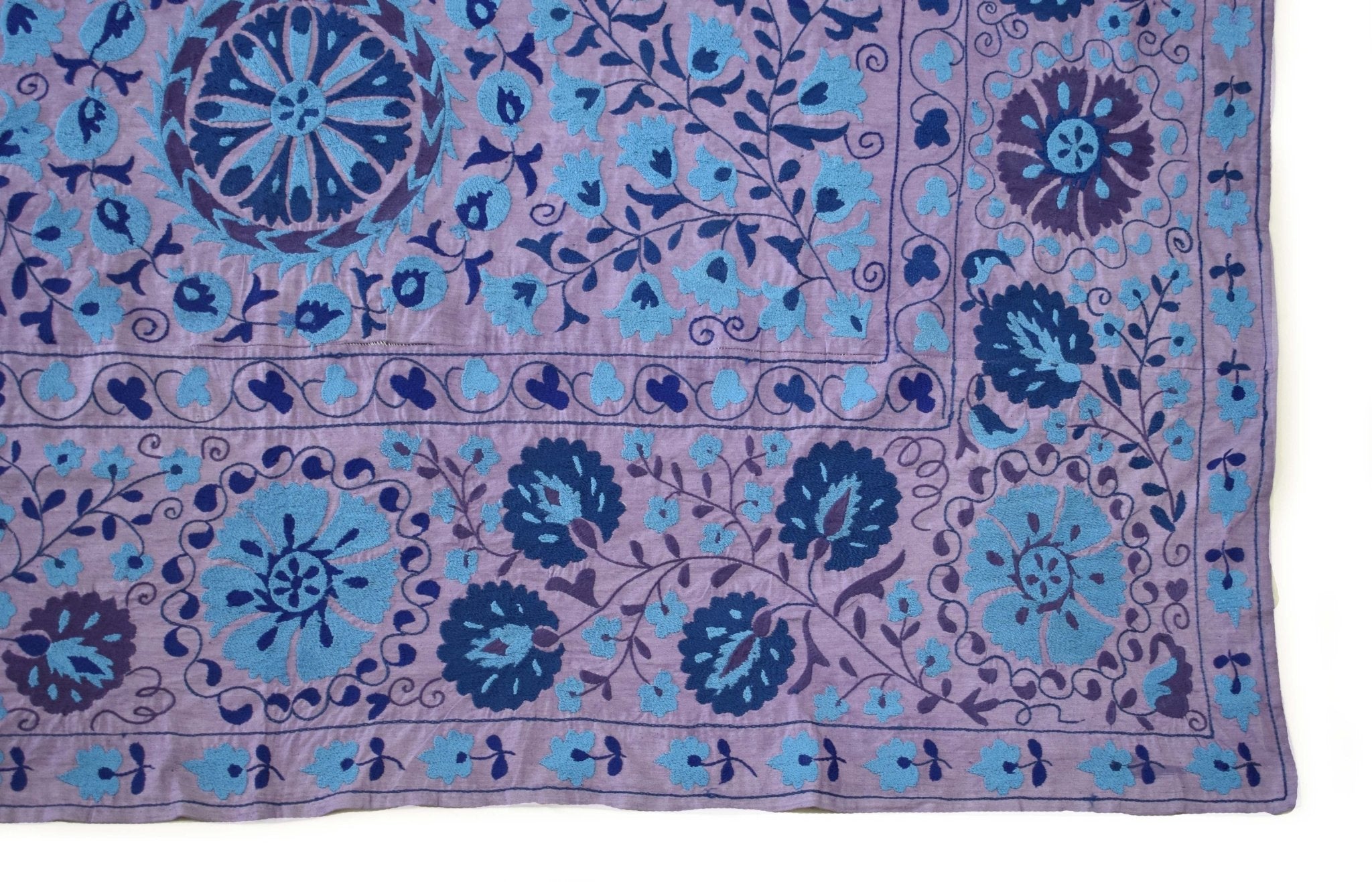 Handmade Uzbek suzani textile featuring blue floral and circular motifs on a purple background.