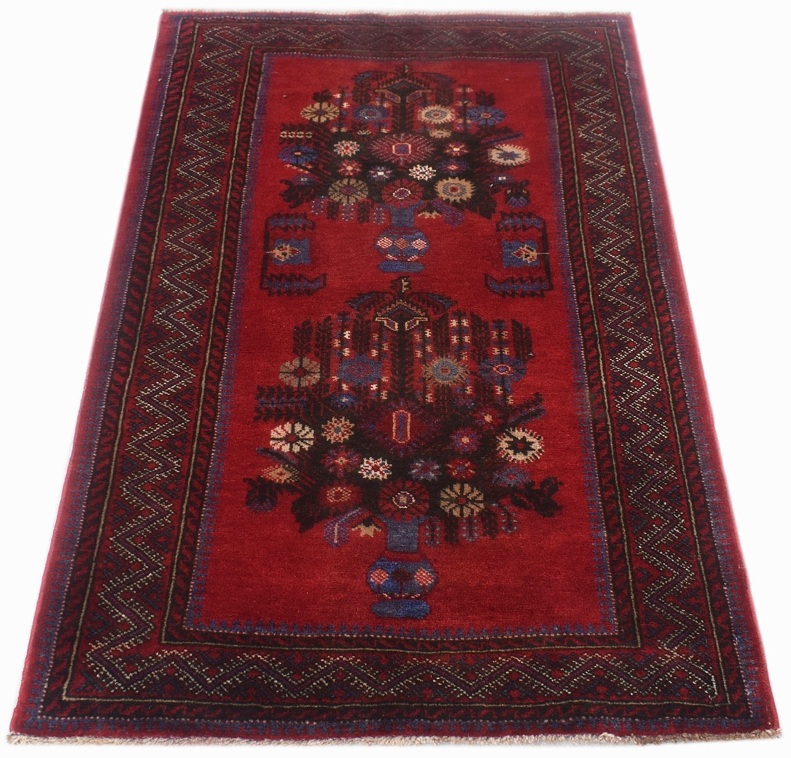 A vintage Afghan Baluch rug featuring two floral vase motifs on a deep red field.