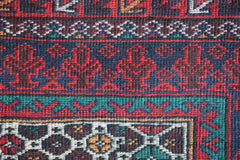 A close-up of a vintage Afghan Baluch rug featuring intricate geometric patterns in red and blue.