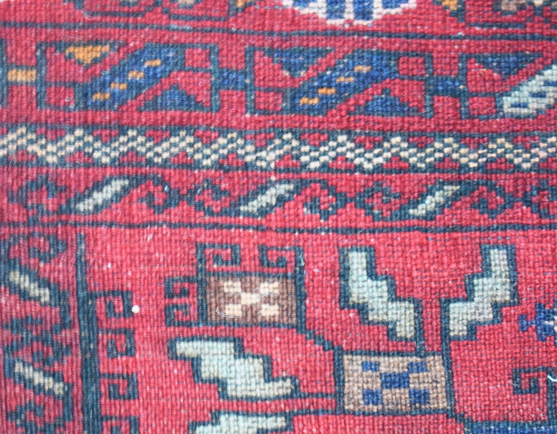 A close-up of a vintage Afghan Baluch rug featuring geometric tribal patterns in red and blue wool.