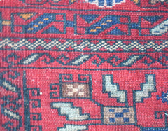 A close-up of a vintage Afghan Baluch rug featuring geometric tribal patterns in red and blue wool.