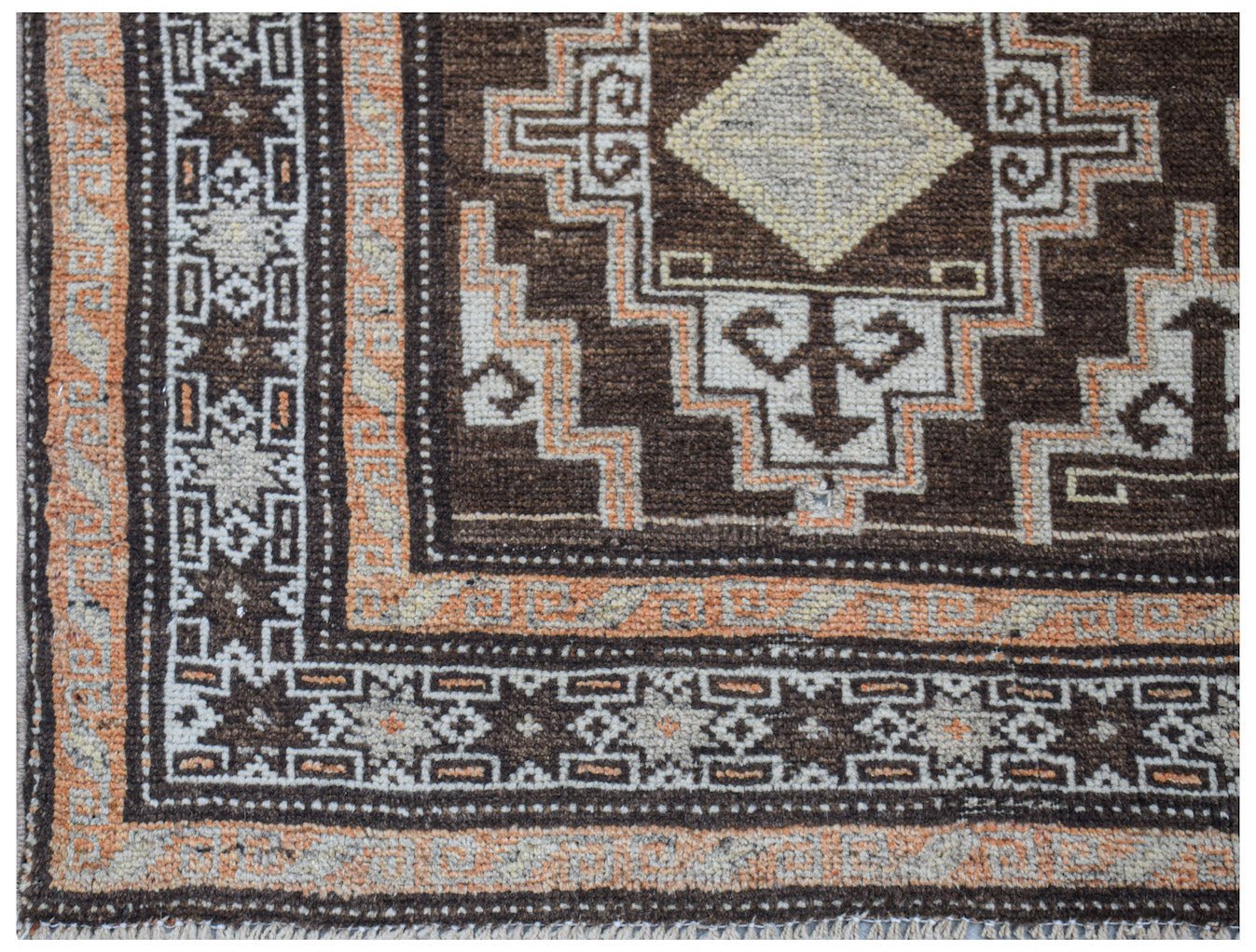 Close-up of a vintage handwoven Afghan Baluch rug with geometric patterns in brown, cream, and orange.
