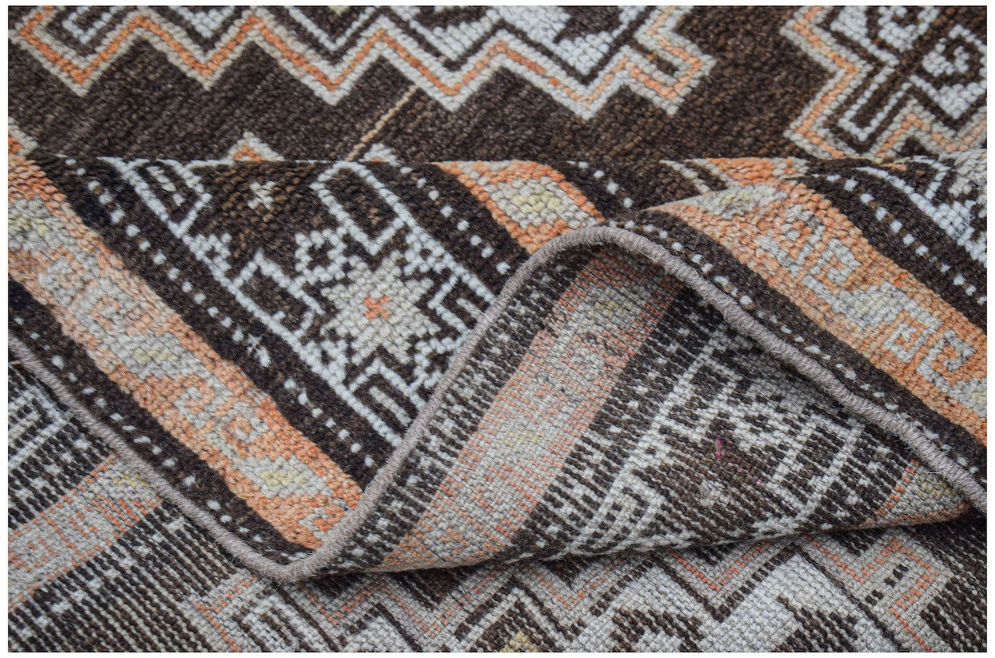 A handwoven vintage Afghan Baluch rug featuring geometric patterns in brown, orange, and cream.