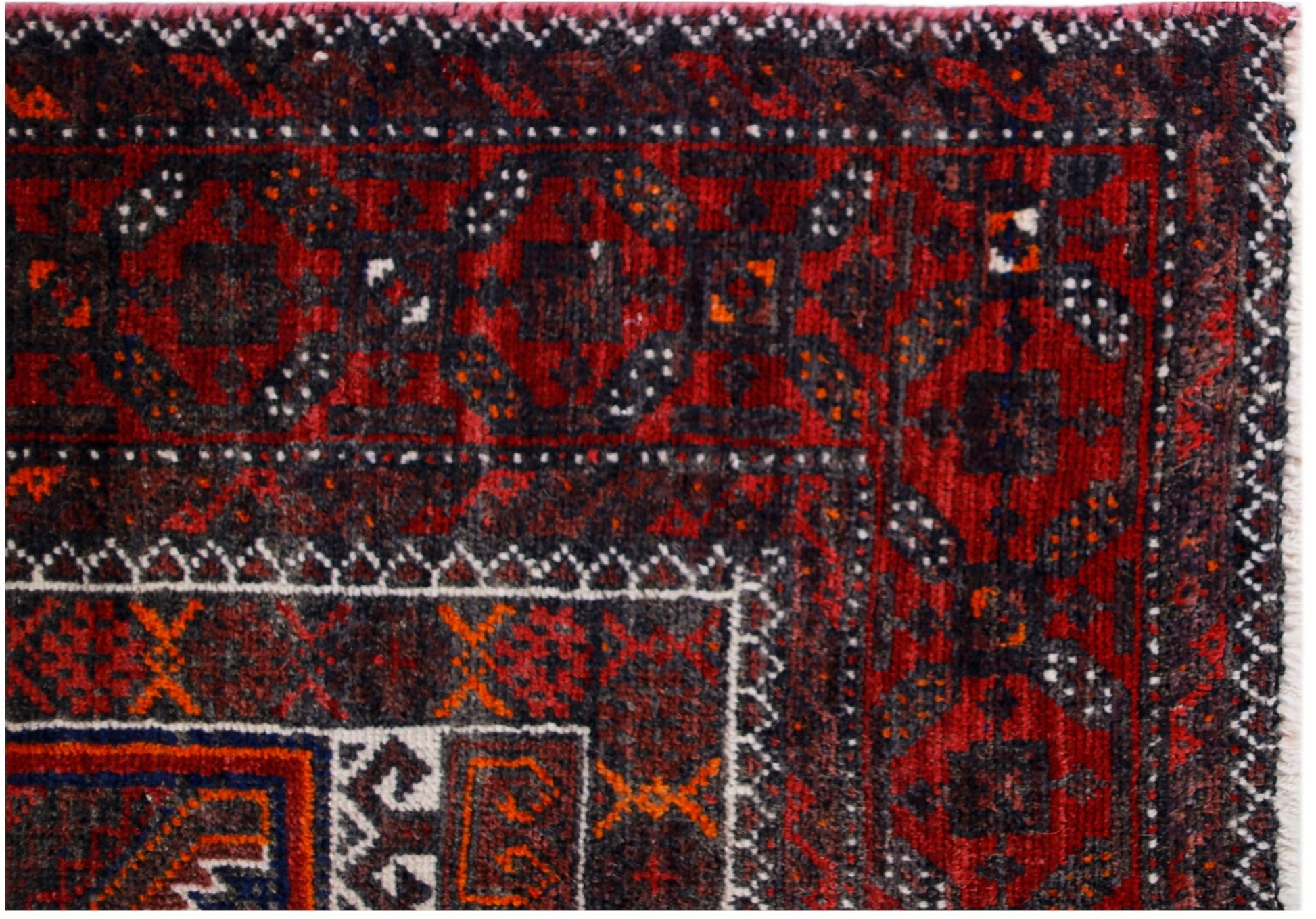 A close-up of a vintage Afghan Baluch rug featuring traditional geometric patterns in red and black.
