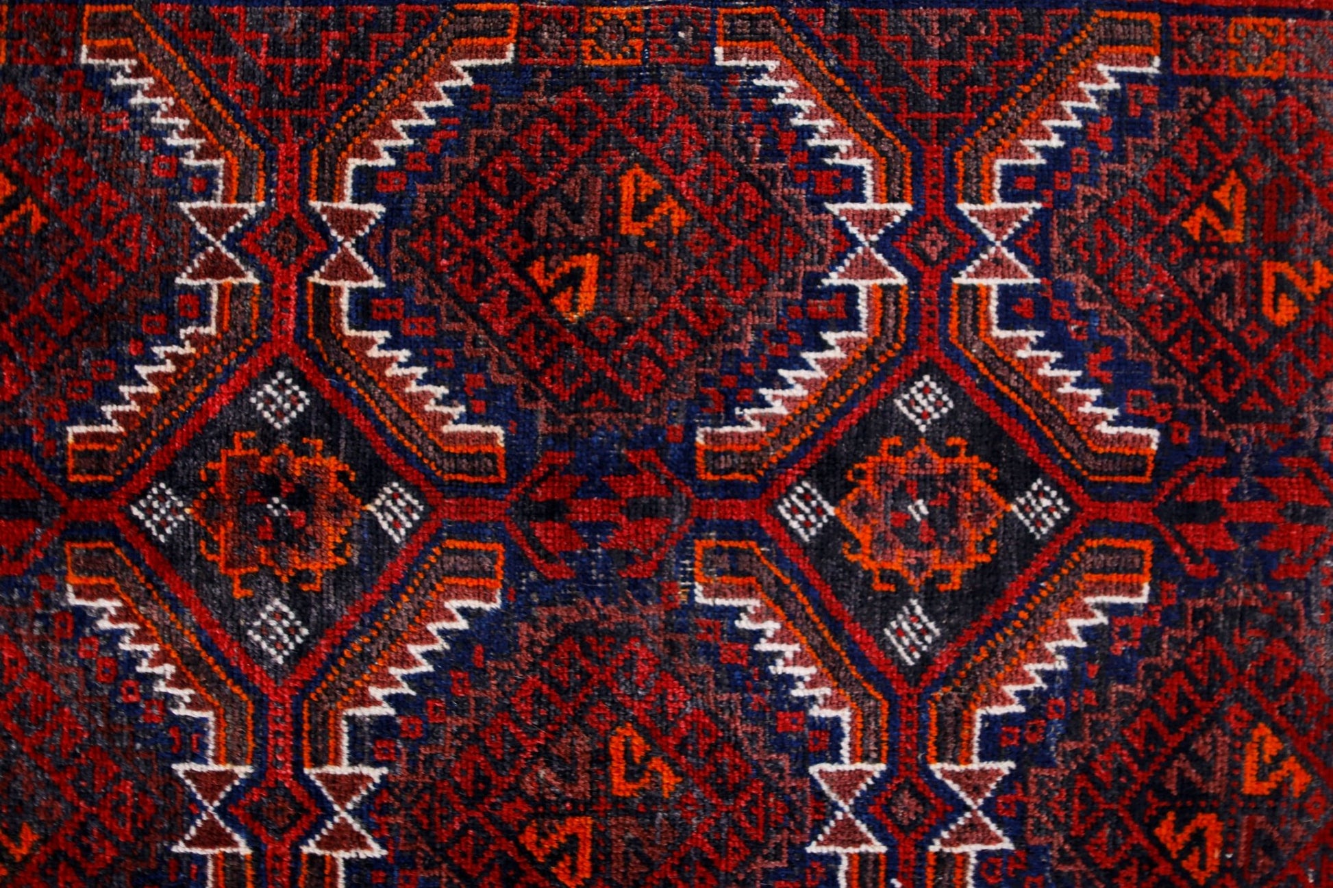 A vintage Afghan Baluch rug featuring a geometric diamond pattern in deep red, blue, and orange.