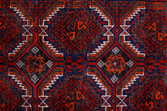 A vintage Afghan Baluch rug featuring a geometric diamond pattern in deep red, blue, and orange.