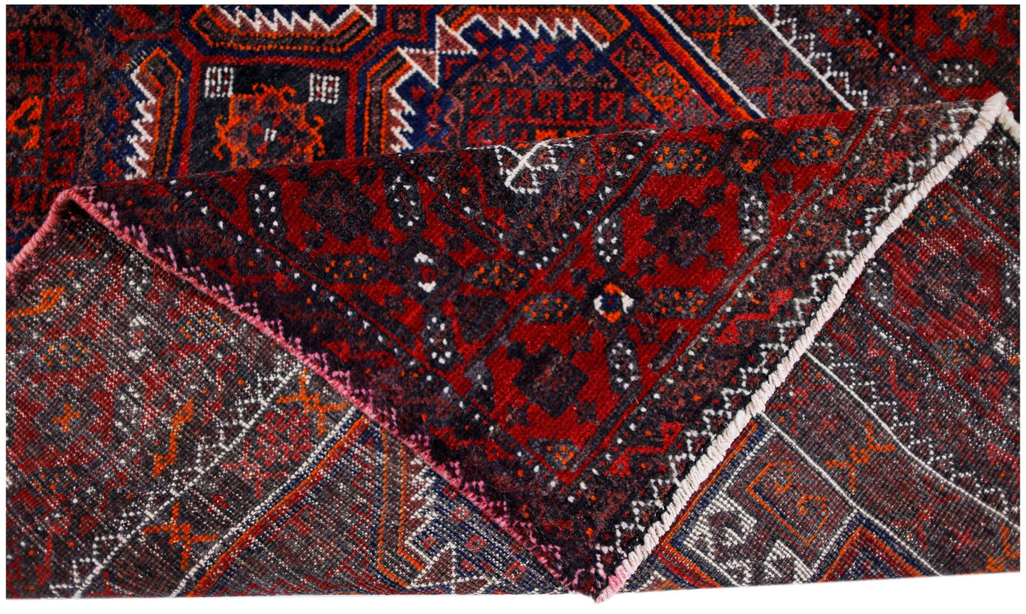 A folded vintage Afghan Baluch rug featuring intricate geometric patterns in red, blue, and black.
