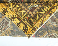 A folded vintage Afghan Baluch rug featuring intricate geometric patterns in brown and yellow tones.