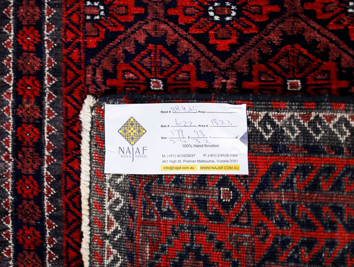 A vintage Afghan Baluch rug featuring a traditional geometric pattern in deep red and black tones.