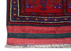 A close-up of a vintage Afghan Baluch rug featuring a red field, blue border, and fringed edge.