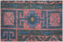 A close-up of a vintage Afghan Baluch rug featuring geometric patterns in red, blue, and black.