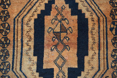 A vintage Afghan Baluch rug featuring a dark blue geometric medallion on a textured orange field.