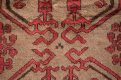 A close-up of a vintage Afghan Baluch wool rug featuring geometric red patterns on a brown field.