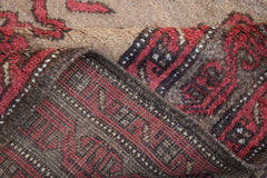 A folded vintage Afghan Baluch wool rug featuring a red and brown geometric tribal pattern.