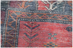A close-up of a vintage Afghan Baluch wool rug featuring geometric patterns in red and blue tones.