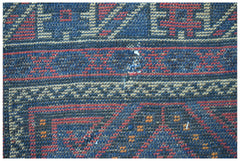 A close-up of a vintage handmade Afghan Baluch wool rug featuring geometric patterns in blue and red.