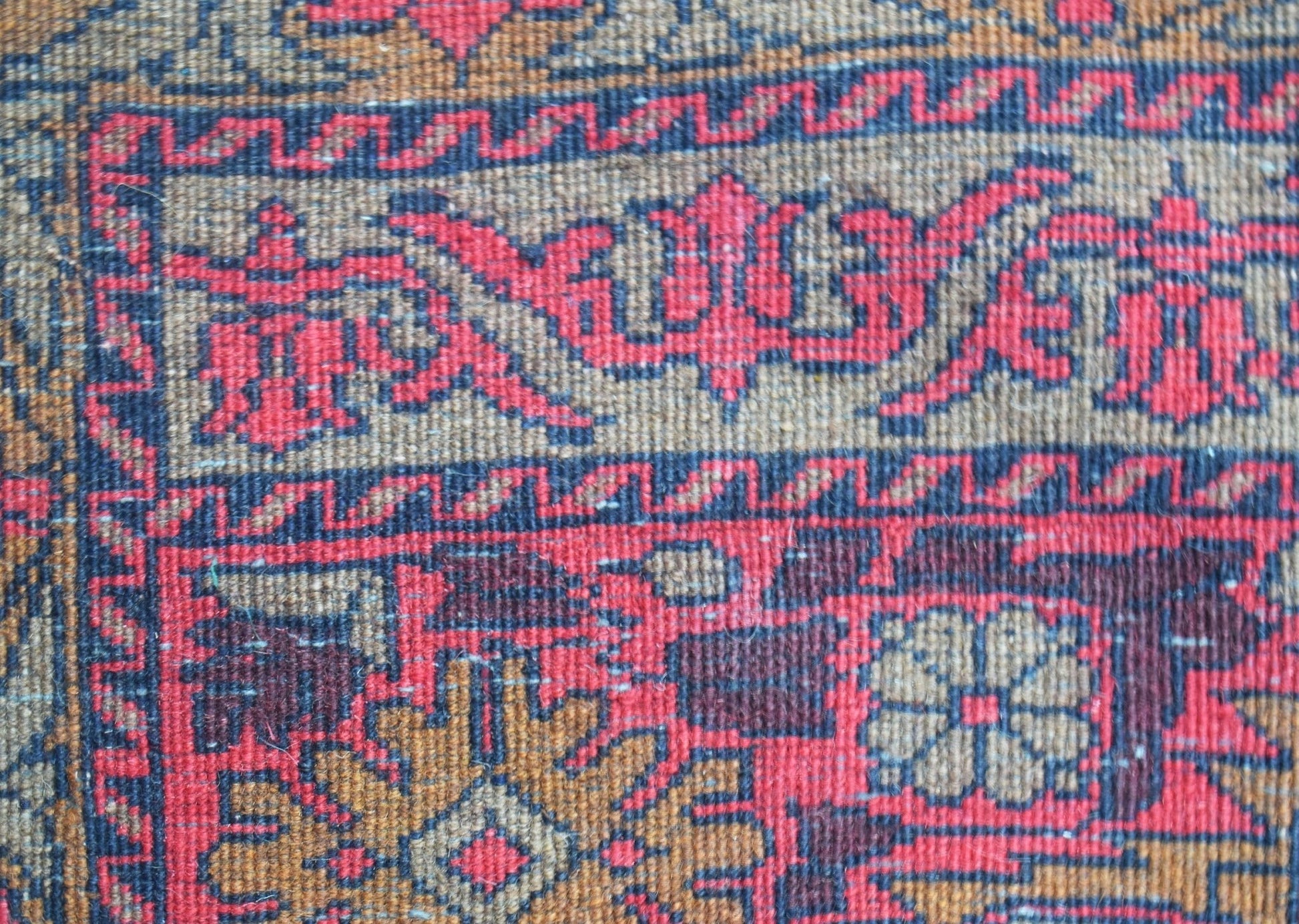 A close-up of a vintage Afghan runner featuring intricate red and brown geometric floral patterns.