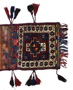 A handmade vintage Afghan wool saddle bag featuring a geometric pattern and decorative tassels.
