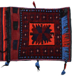 A vintage handmade Afghan wool saddle bag featuring a central geometric motif and blue fringe.