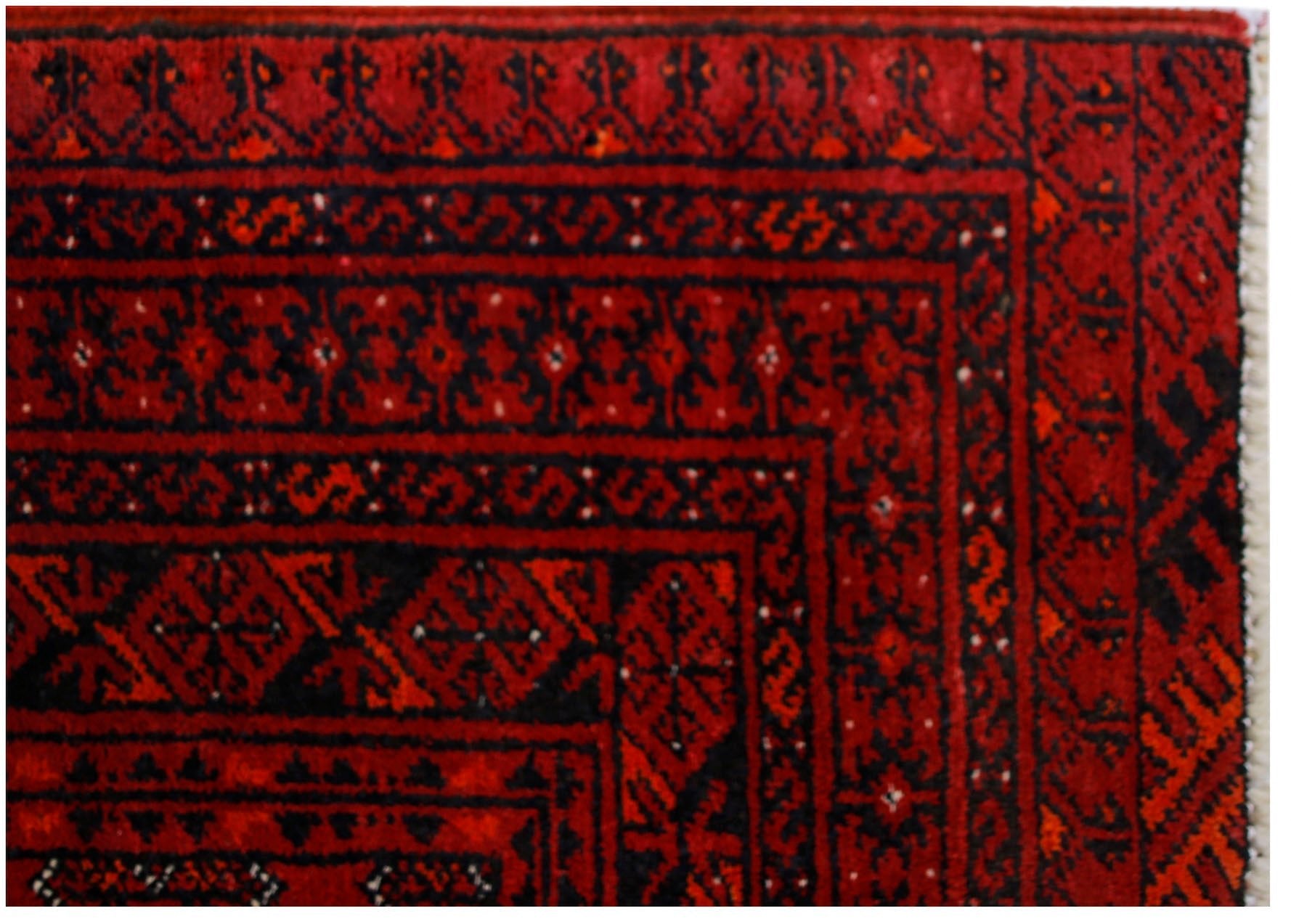 A vintage Afghan Turkmen rug featuring traditional geometric patterns in deep red and black.