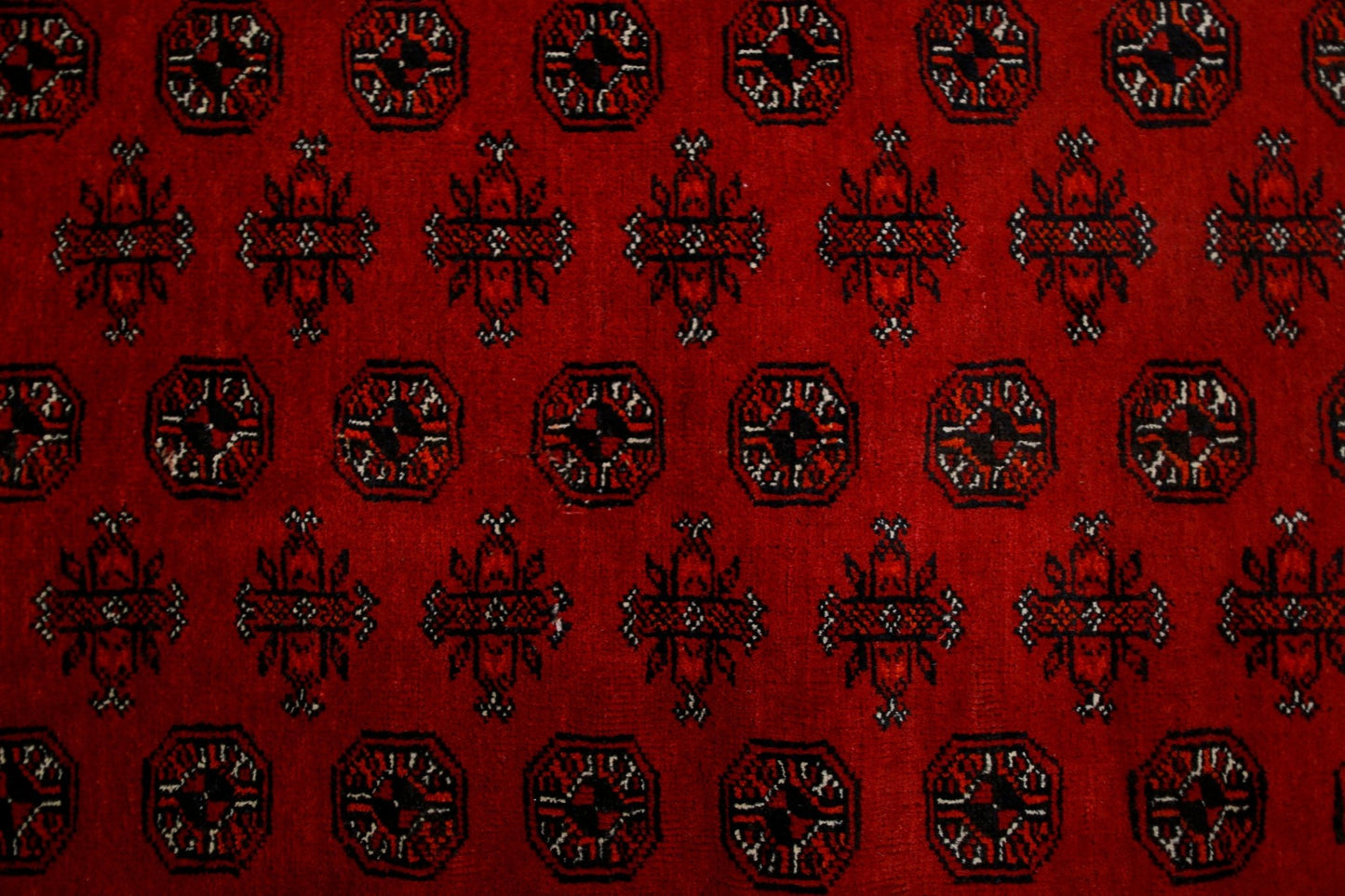 A vintage Afghan Turkmen rug featuring a repeating pattern of octagons and floral motifs in red.