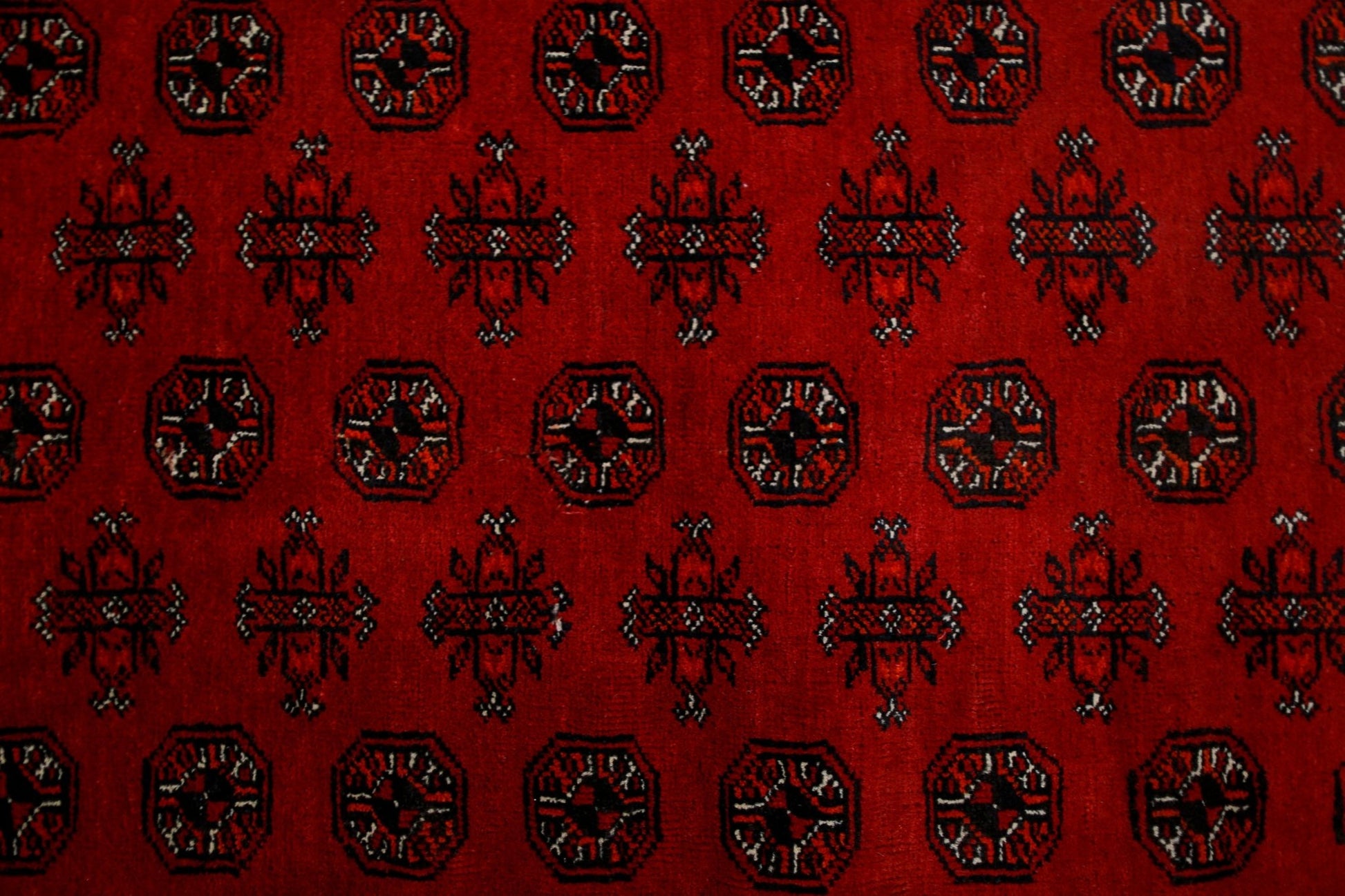 A vintage Afghan Turkmen rug featuring a repeating pattern of octagons and floral motifs in red.