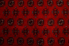 A vintage Afghan Turkmen rug featuring a repeating pattern of octagons and floral motifs in red.