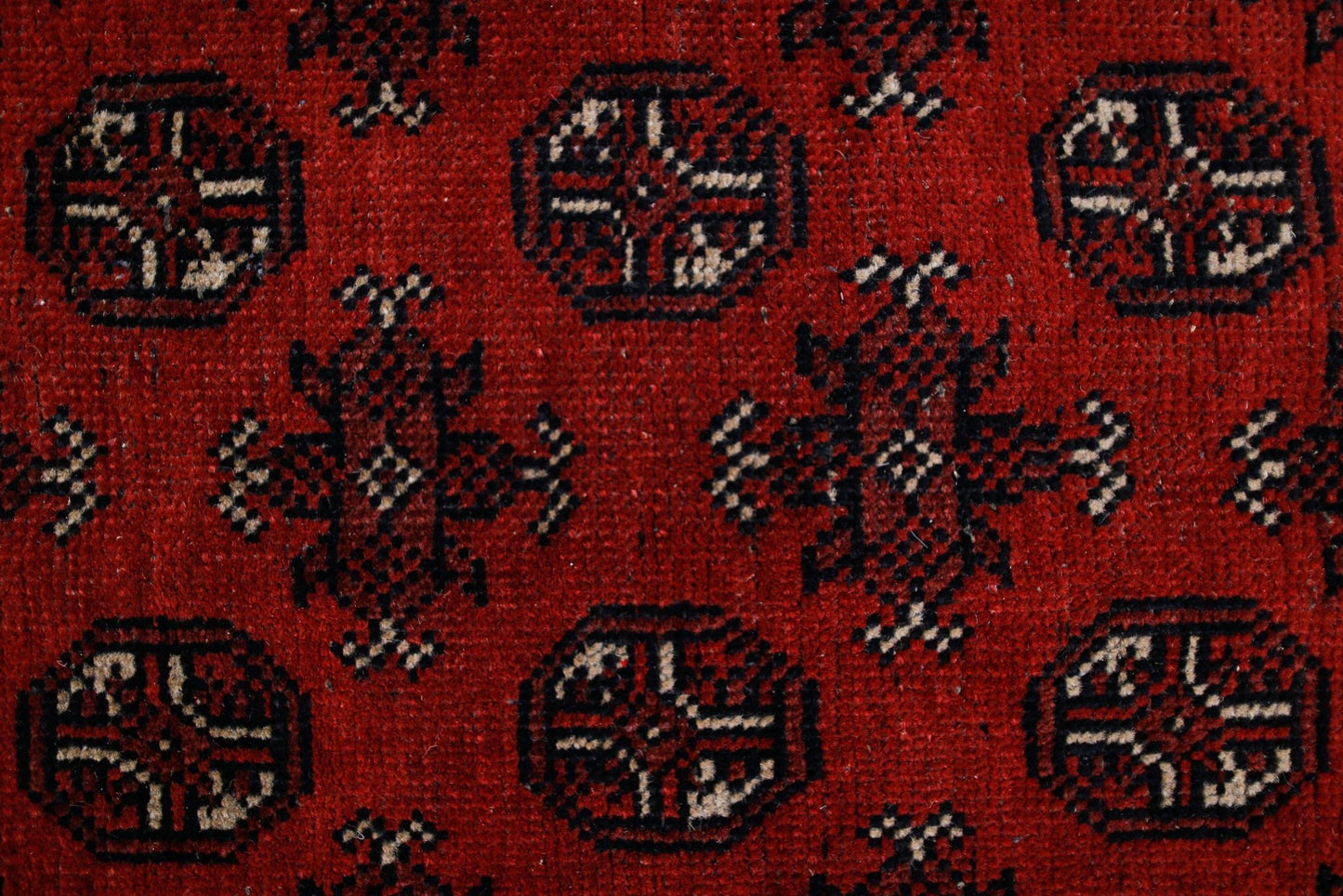 A vintage Afghan Turkmen rug featuring a repeating geometric pattern in deep red and black wool.