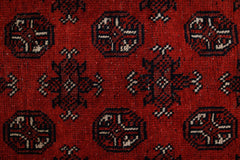 A vintage Afghan Turkmen rug featuring a repeating geometric pattern in deep red and black wool.