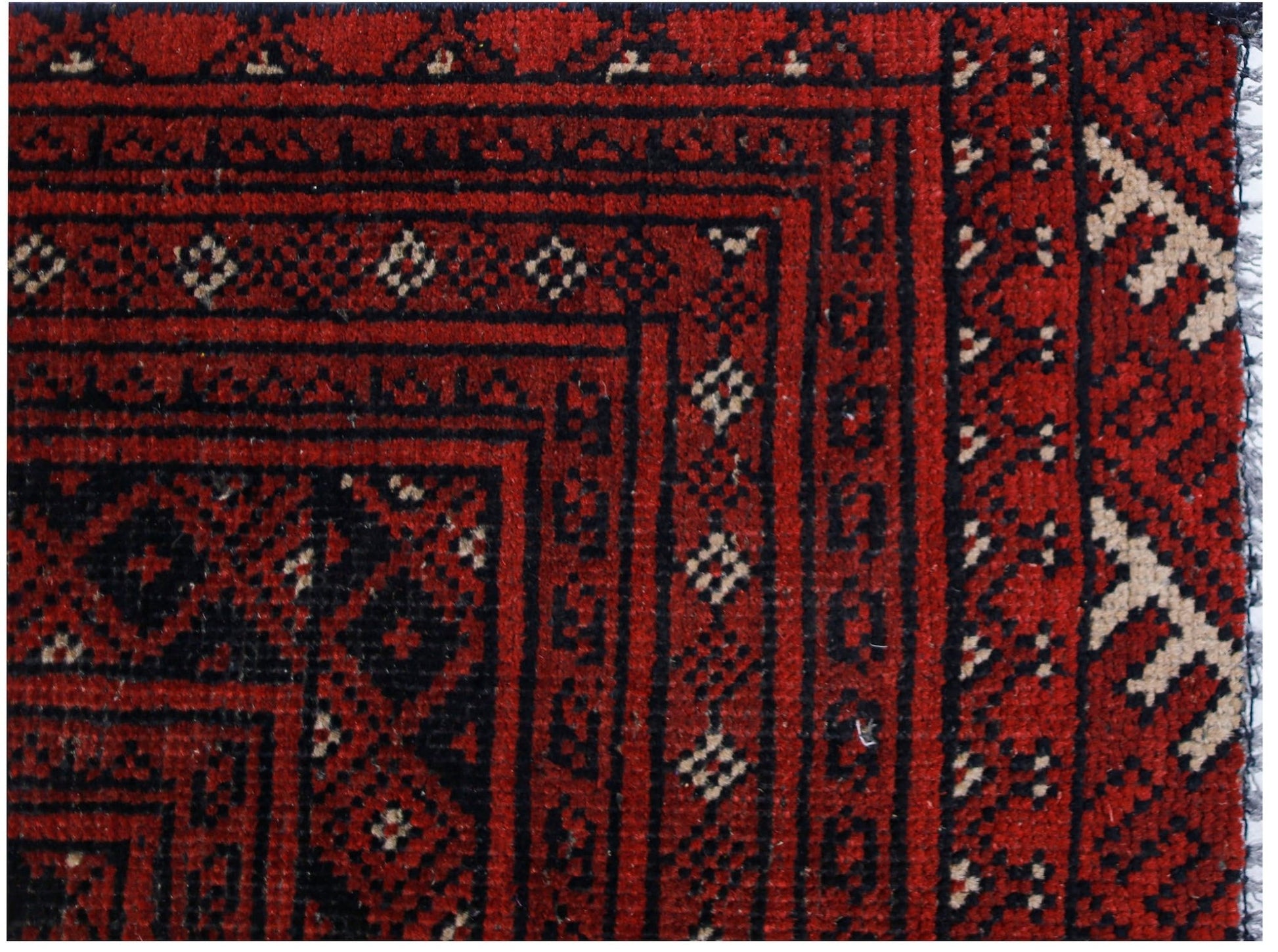A close-up of a vintage Afghan Turkmen rug featuring intricate geometric patterns in red and black.