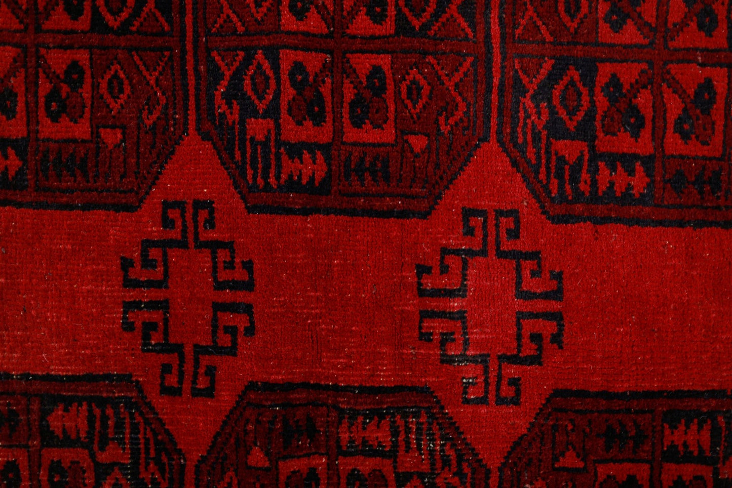 A vintage Afghan Turkmen rug featuring a geometric pattern in deep red and black wool.