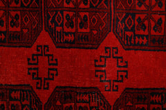 A vintage Afghan Turkmen rug featuring a geometric pattern in deep red and black wool.