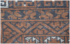 A close-up of a vintage Afghan Turkmen rug featuring intricate geometric patterns in brown and black.