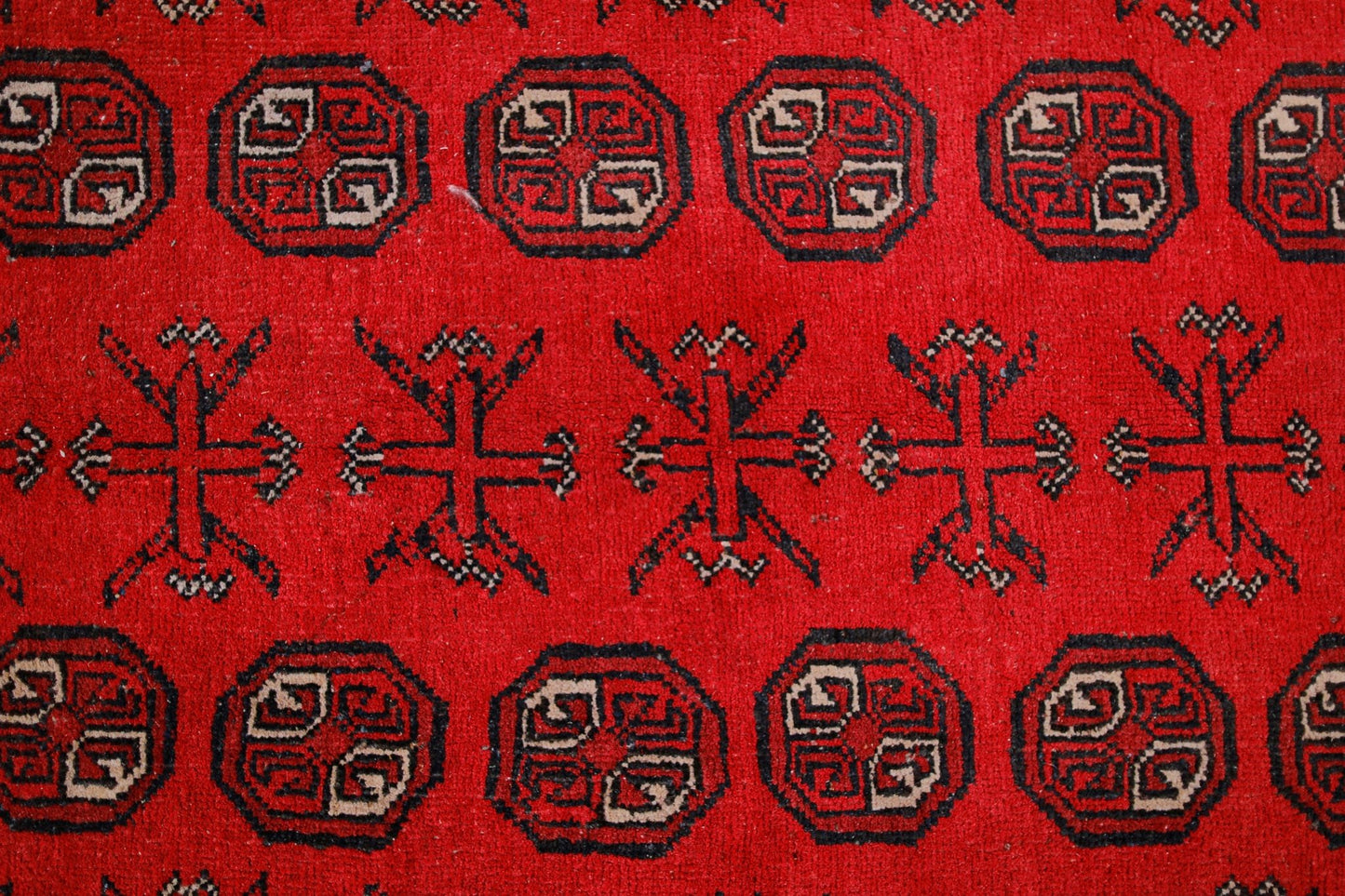 A vintage Afghan Turkmen rug featuring repeating geometric octagons and cross motifs in red.