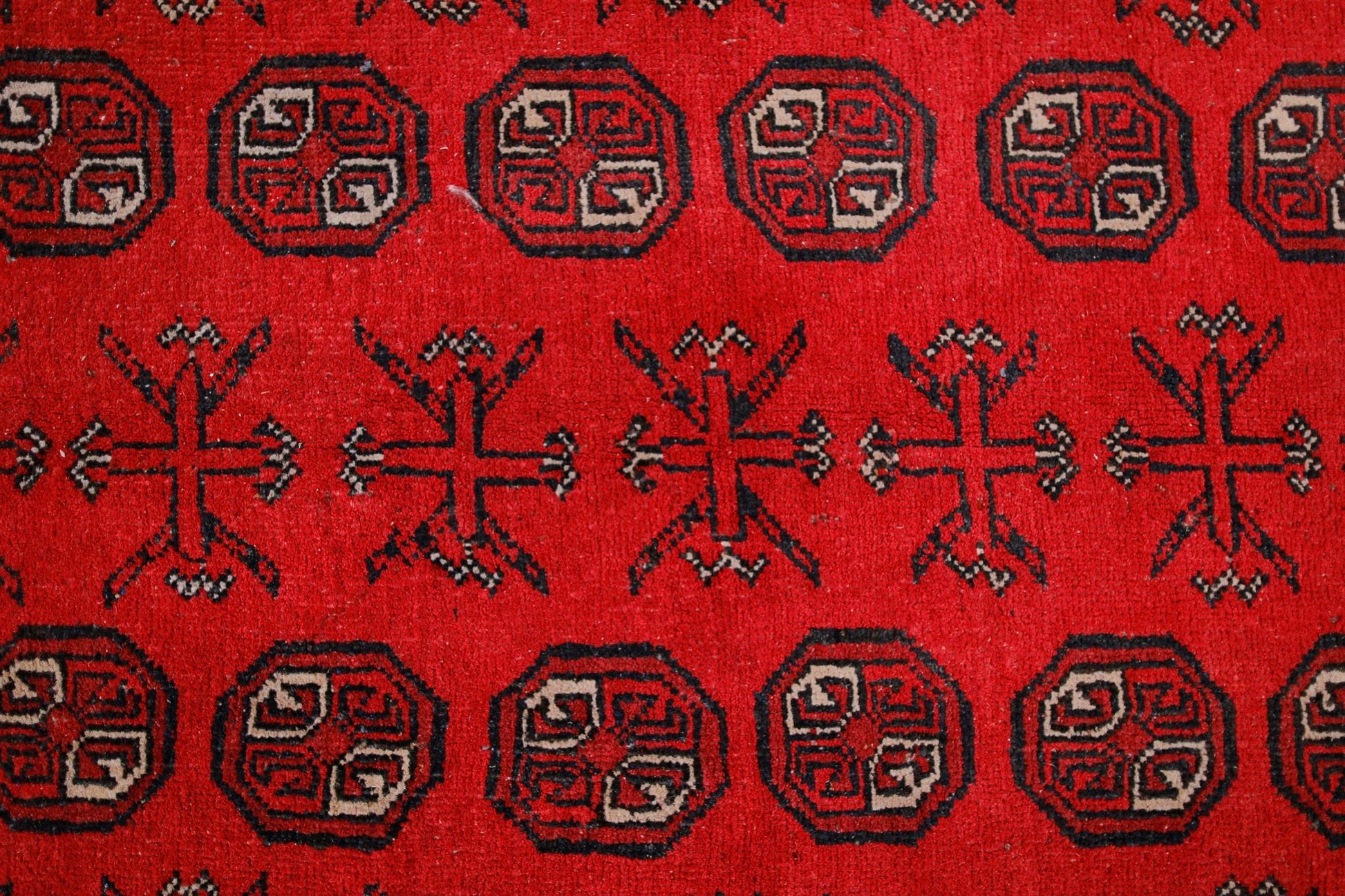 A vintage Afghan Turkmen rug featuring repeating geometric octagons and cross motifs in red.
