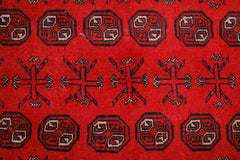 A vintage Afghan Turkmen rug featuring repeating geometric octagons and cross motifs in red.