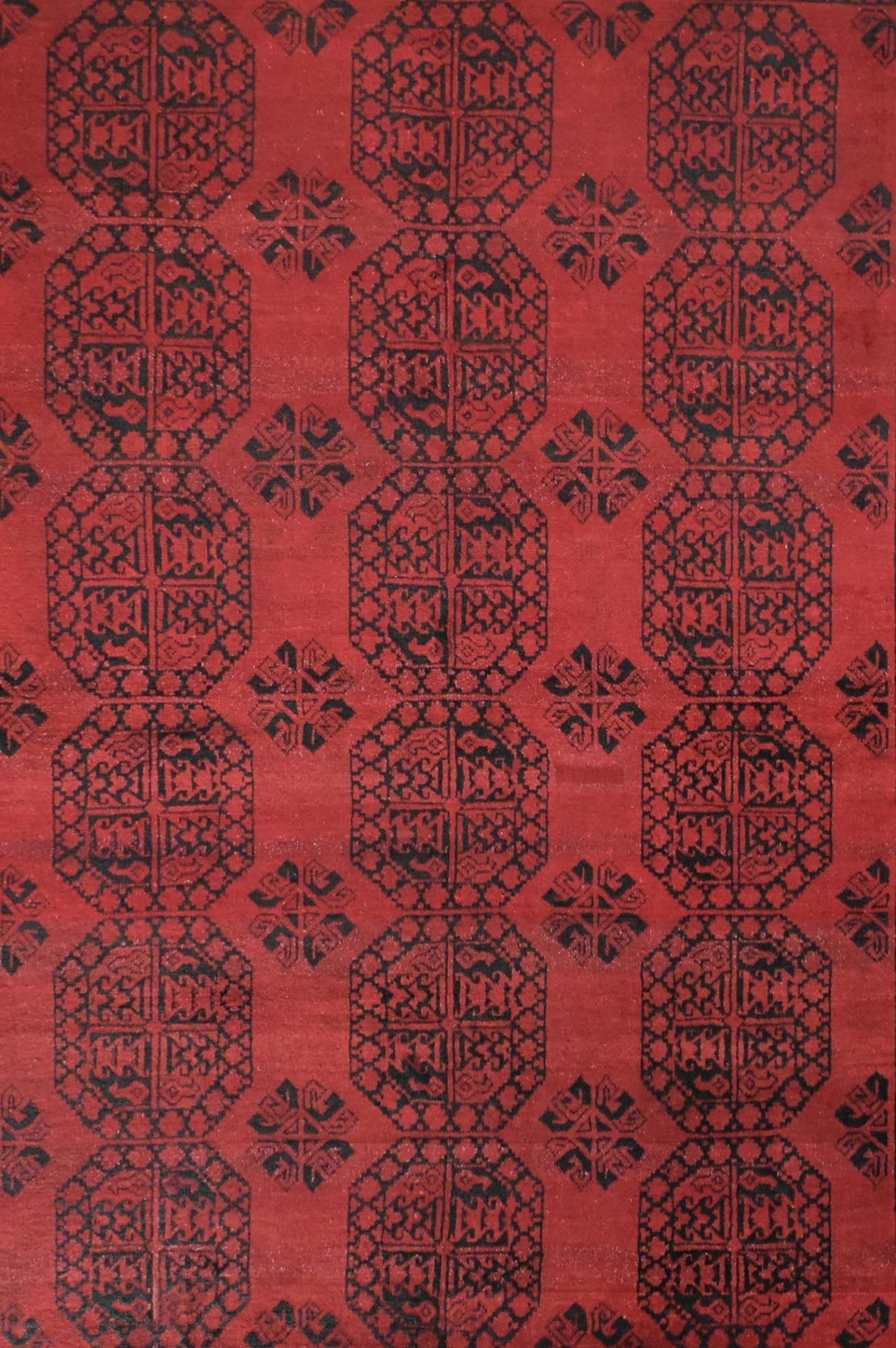 A vintage handmade Afghan Turkmen rug featuring a repeating geometric pattern in black on red.