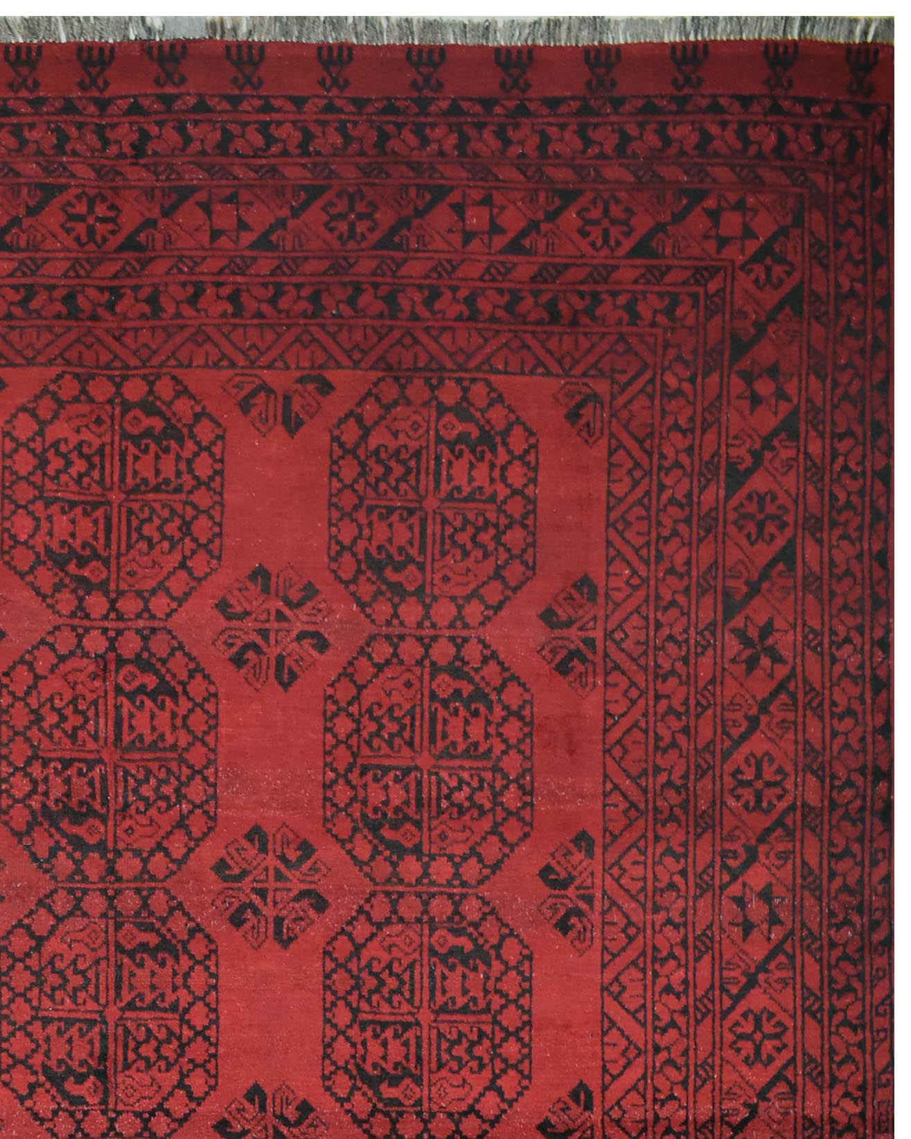 A vintage Afghan Turkmen rug featuring a deep red background with black geometric patterns.