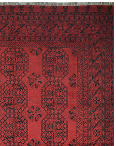 A vintage Afghan Turkmen rug featuring a deep red background with black geometric patterns.