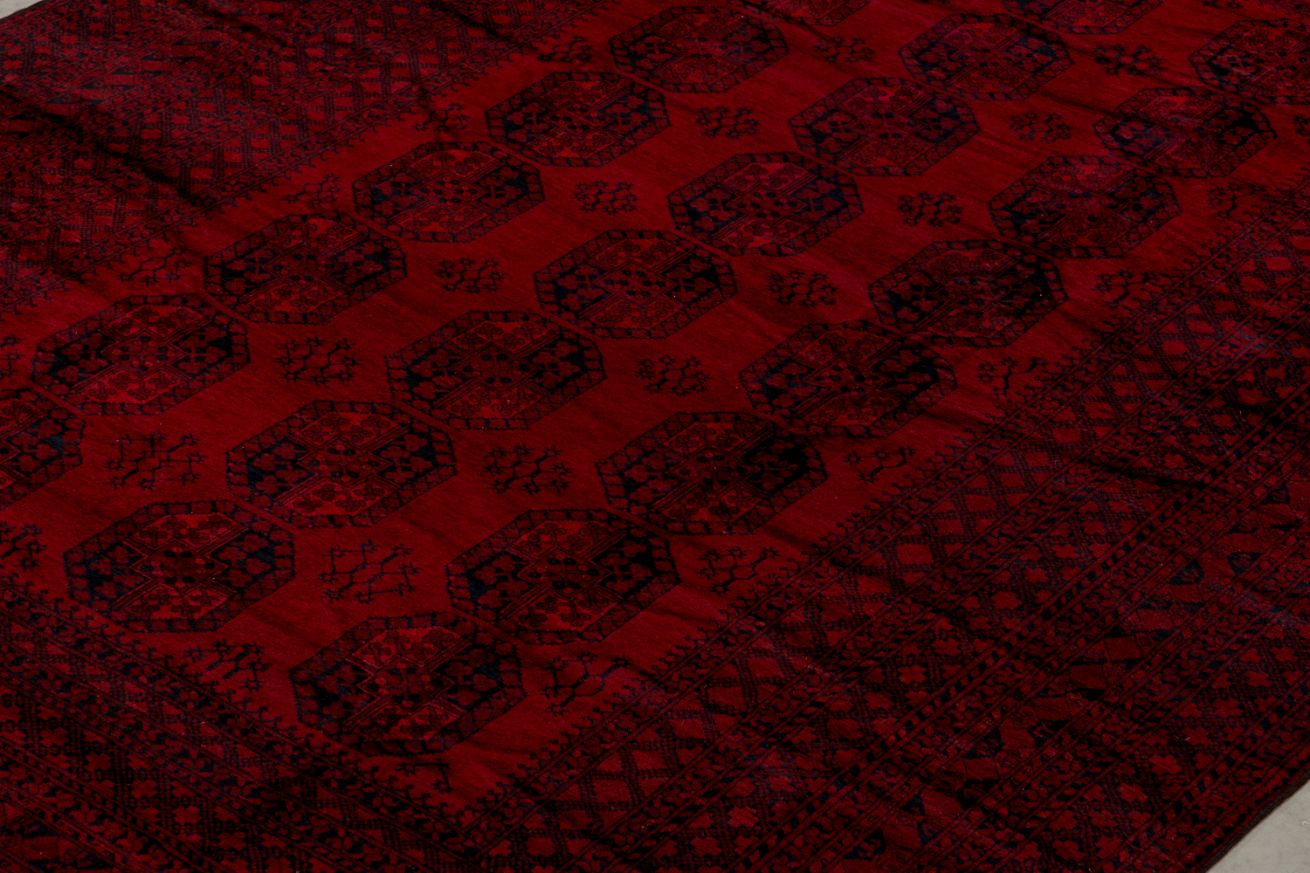 A vintage handmade Afghan Turkmen rug featuring a deep red field with repeating geometric motifs.