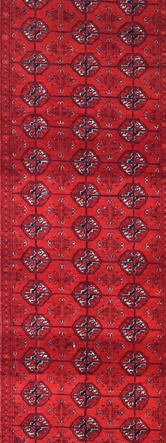 A vintage Afghan Turkmen runner rug featuring a repeating geometric pattern in deep red tones.